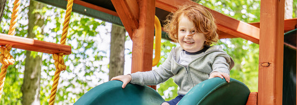 child sliding down backyard wooden playsets - read more about playground safety tips
