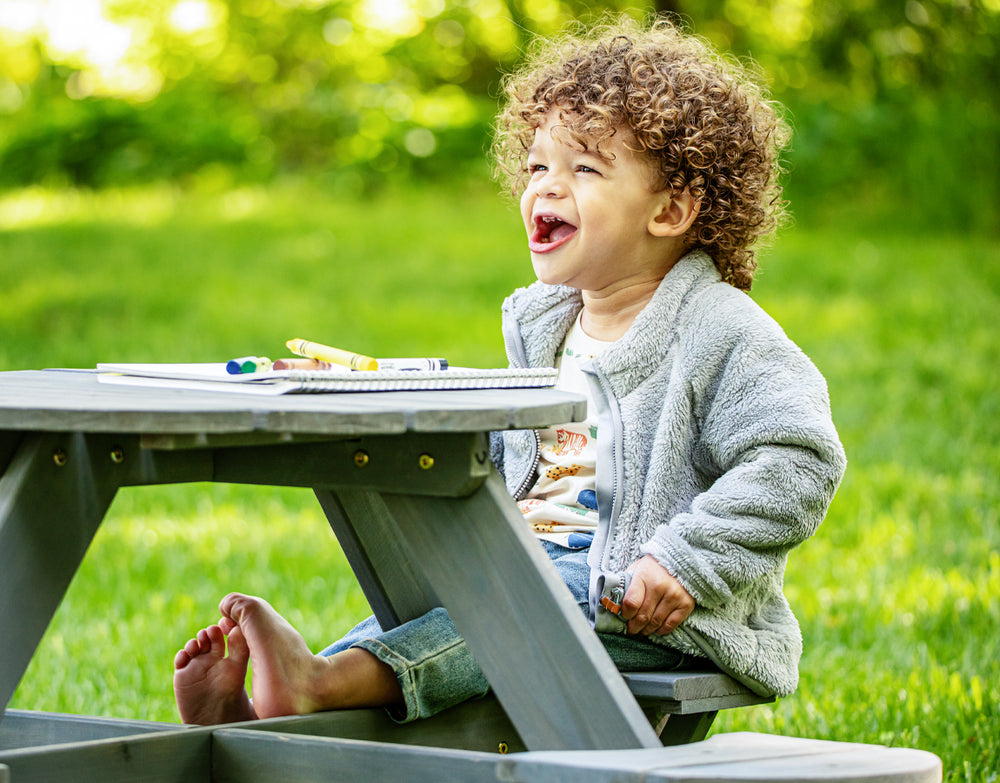 child laughing while coloring at outdoor wooden picnic table