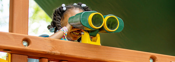 little girl looking through binoculars on backyard wooden playset
