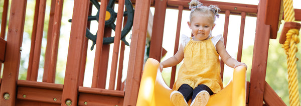 how to care for your playset: little girl sliding down backyard wooden playsets