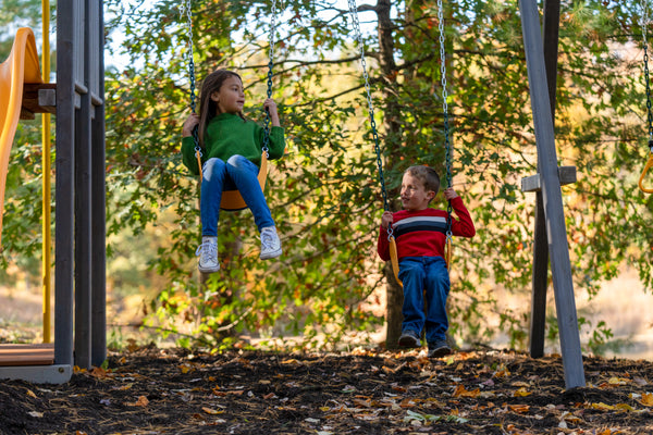 two kids swinging on a swingset in fall weather